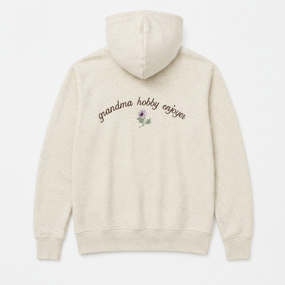 Oatmeal hoodie with 'grandma hobby enjoyer' text and flower design on a white background