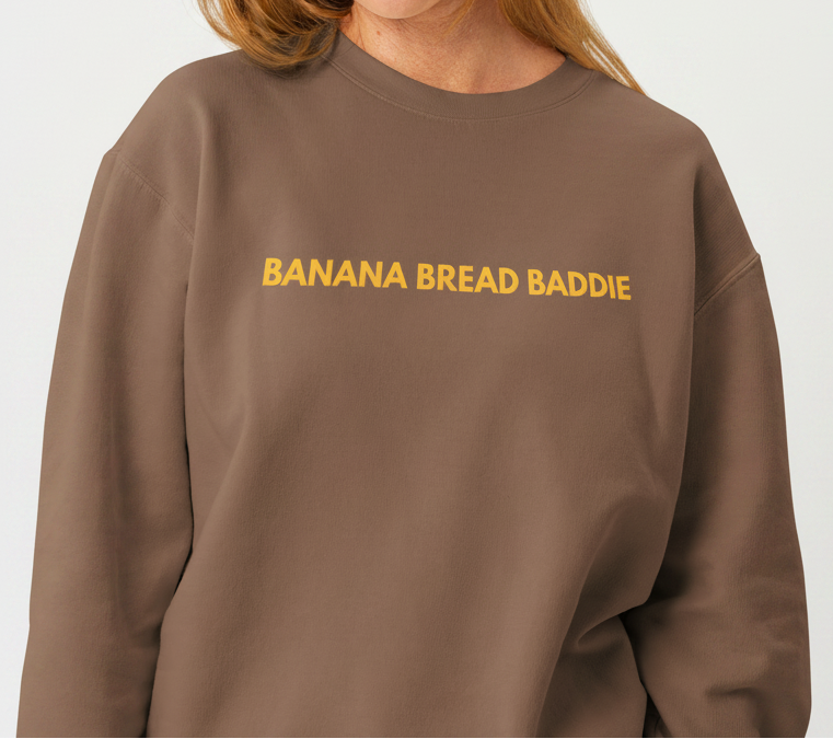 Woman wearing a brown sweatshirt with 'BANANA BREAD BADDIE' text on a white background